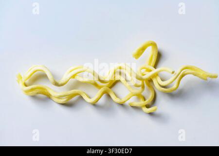 Una vista dettagliata di alcuni fili di noodles istantanei gialli, ondulati e crudi disposti su una superficie bianca e pulita, perfetti per i temi alimentari e culinari Foto Stock