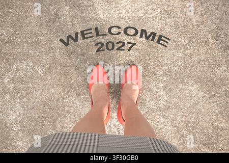 Messaggio „Benvenuti nel 2027“ davanti a una donna che indossa tacchi arancioni. Vista dall'alto. Foto Stock