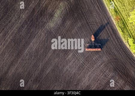 Vista predefinita di attrezzature per la semina in funzione su terreni agricoli coltivati. Una grande area aperta di terreno arato fornisce spazio per testo, pubblicità o des Foto Stock