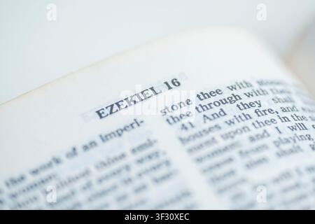 Un macroscatto a fuoco selettivo di una pagina aperta della Bibbia con il titolo del capitolo Ezechiele 16, che mostra dettagli di testo con una bassa profondità di campo Foto Stock