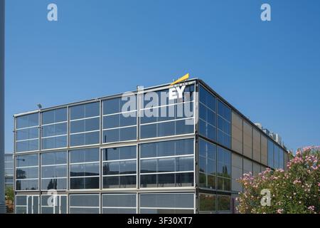 grattacielo moderno con logo EY, su uno sfondo di cielo azzurro e circondato da una vegetazione lussureggiante, che rappresenta l'eccellenza e l'innovazione aziendale Foto Stock