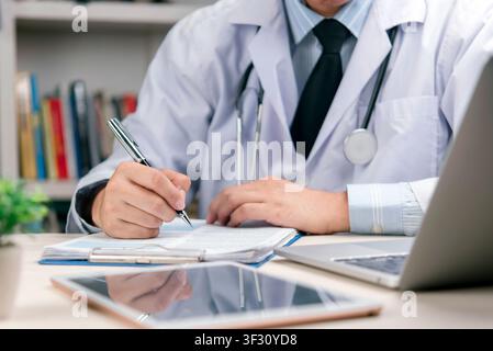 Primo piano di un medico maschio che prende appunti su un rapporto cartaceo. Medico che utilizza tecnologia e penna per la diagnosi in clinica. Studio medico e amministrazione Foto Stock