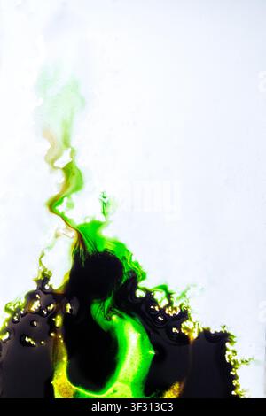 Vibrante inchiostro verde neon e nero scuro che reagisce e si diffonde su una superficie bianca, creando forme organiche fluide. Perfetto per l'arte astratta, la scienza o Foto Stock