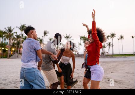 Amici energici che celebrano una festa estiva sulla spiaggia al tramonto, incarnando la vacanza spensierata Foto Stock