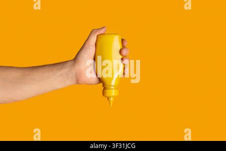 Bottiglia spremiagrumi a mano maschile con senape su fondo arancione, primo piano. Spazio per il testo Foto Stock
