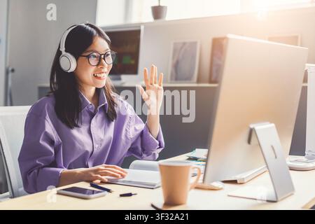 Donna asiatica sorridente con cuffie che lavora in ufficio a casa, concetto aziendale Foto Stock