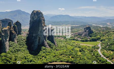 Vista a drone delle massicce formazioni rocciose delle Meteore vicino al villaggio di Kastraki in Tessaglia, Grecia, circondate da una fitta foresta verde in una giornata estiva soleggiata sotto un cielo blu Foto Stock