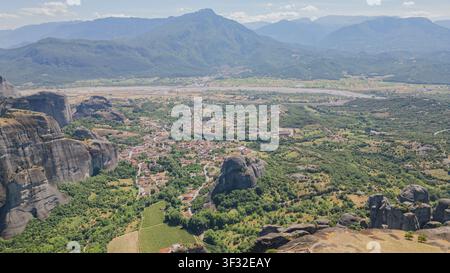 Scatto panoramico con drone delle formazioni rocciose delle Meteore e del villaggio di Kastraki nella valle con una catena montuosa in lontananza sotto un cielo blu nella regione della Tessaglia in Grecia in su Foto Stock