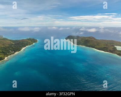 Vista aerea di una tranquilla baia turchese incastonata tra due colline rigogliose, che si apre sull'oceano infinito. Praslin, Seychelles. Foto Stock