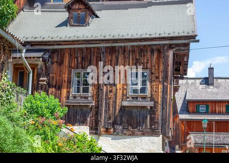 Facciata in legno rustica di una casa alpina tradizionale con piccole finestre e fiore. Villaggio Hallstatt Austria Foto Stock