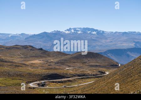 Una strada asfaltata tortuosa si snoda attraverso le colline aride ad alta quota delle Ande peruviane, con vista sulla maestosa catena montuosa del Mismi Foto Stock