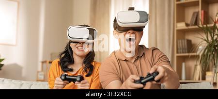 Uomo e donna asiatici felici che giocano ai videogiochi con cuffie VR a casa, atmosfera allegra Foto Stock