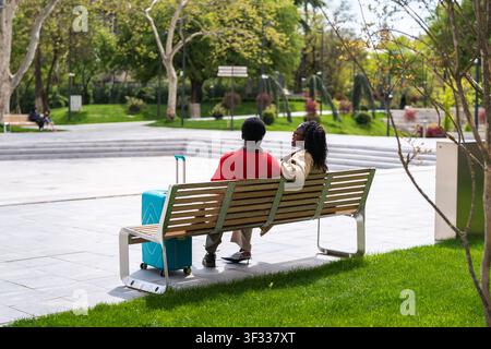 Coppia afro-americana, uomo e donna, turisti che si rilassano in un giardino cittadino godendosi una conversazione spensierata. Foto Stock