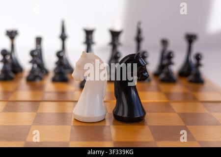 Cavalliere di scacchi bianchi e neri su una classica scacchiera di legno con pezzi sfocati sullo sfondo. Simbolo di strategia, rivalità e competizione intellettuale f Foto Stock