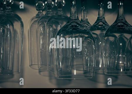 Macro primo piano di bicchieri di vino in cristallo capovolti appesi in fila con toni cinematografici scuri e atmosferici e riflessi Foto Stock