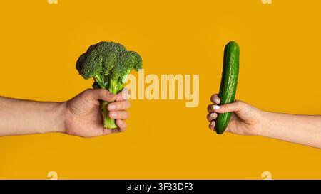 Mangiare sano. Primo piano di uomo che tiene broccoli e donna con cetriolo, fondo arancione. Panorama Foto Stock