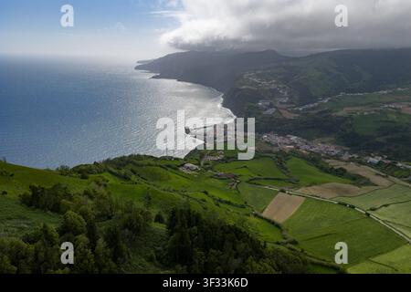 Vista aerea della lussureggiante costa verde e della piccola città arroccata contro l'Oceano Atlantico a Povoacao, Azzorre, Portogallo. Foto Stock