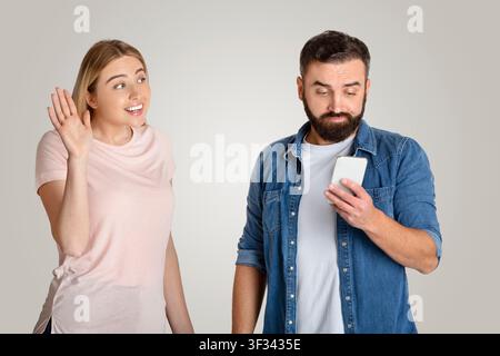 Giovane donna felice che saluta un uomo mentre usa lo smartphone, sfondo dello studio Foto Stock