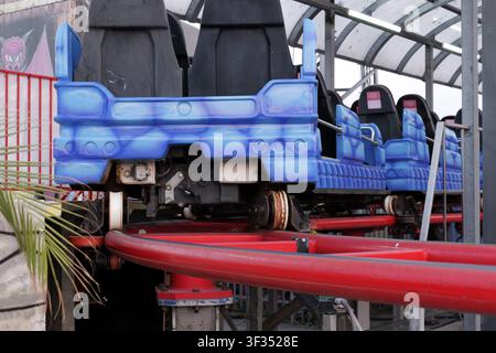 Vagoni blu di una montagna russa del parco divertimenti appoggiati sui binari rosso acceso, in attesa di trasportare i passeggeri in un giro emozionante con velocità e brividi Foto Stock
