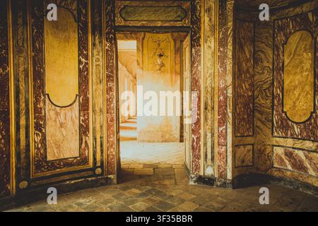 AGLIÈ, ITALIA – OTTOBRE 2025: Vista interna del castello di Agliè con pareti dipinte ornate, marmi invecchiati e porte che conducono a un corrido illuminato dal sole Foto Stock