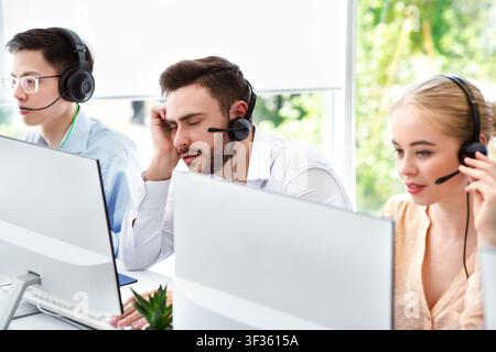 Un rappresentante del call center stanco e i suoi colleghi al lavoro ufficio open space Foto Stock