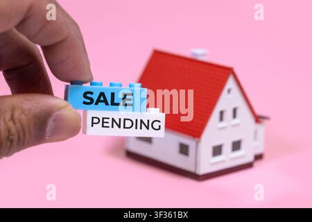 Mano che tiene blocchi di costruzione in attesa di vendita davanti a una casa in miniatura Foto Stock