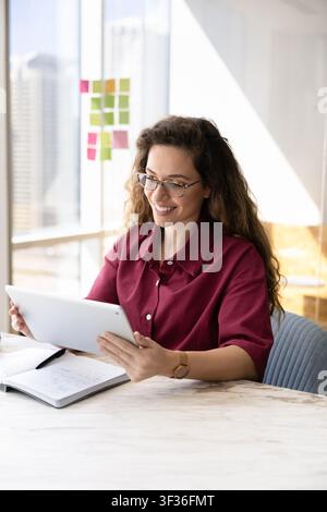 Dipendente donna sorridente che tiene un tablet digitale alla scrivania dell'ufficio Foto Stock