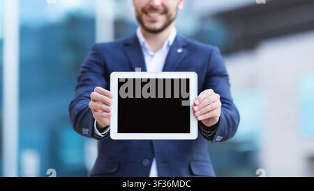 Vista in primo piano di un giovane uomo d'affari che mostra un computer tablet con schermo vuoto sulla strada della città, mockup per il tuo design Foto Stock