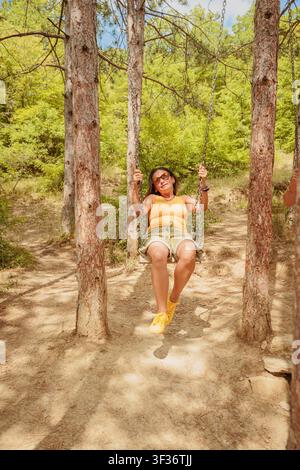 Donna matura con occhiali da sole che si gode un momento tranquillo cullando nel bosco in una giornata di sole Foto Stock