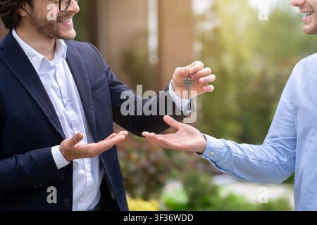 Vista ritagliata dell'agente immobiliare che dà la chiave della casa al nuovo proprietario della casa vicino alla sua proprietà, primo piano Foto Stock