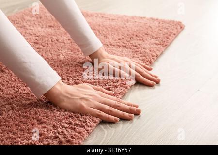Mani di una donna che toccano un tappeto soffice e shaggy rosa pallido su un pavimento di legno chiaro, arredamento e comfort Foto Stock