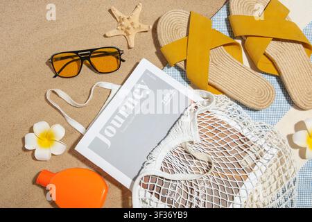 Borsa a cordoncino con bottiglia di crema solare, caricatore e accessori da spiaggia sulla sabbia come sfondo, primo piano Foto Stock