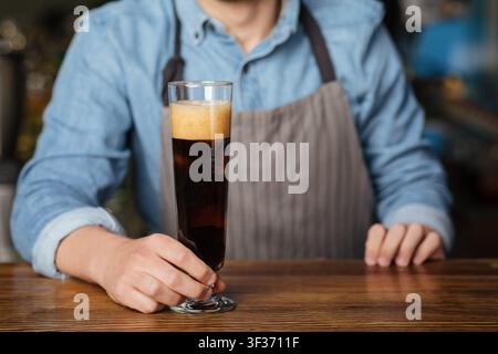 Ale scuro con schiuma. Il barman tiene un bicchiere di birra alto sul banco bar in legno Foto Stock