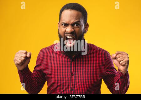 Uomo arrabbiato afro che urla con i pugni alzati Foto Stock