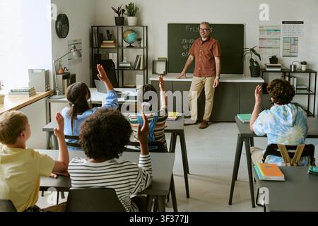 Studenti adolescenti diversificati che alzano le mani durante una lezione di matematica in classe Foto Stock