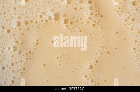 Prima vista della texture di un frullato di mango. Sfondo di schiuma di frullato all'arancia, foto macro di bolle di frullato di frutta, vista dall'alto di un cocktail schiumoso e latteo montato Foto Stock