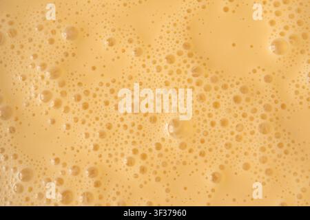 Prima vista della texture di un frullato di mango. Sfondo di schiuma di frullato all'arancia, foto macro di bolle di frullato di frutta, vista dall'alto di un cocktail schiumoso e latteo montato Foto Stock