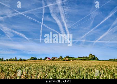 Sciie di vapore / scie di condensa che si incrociano in un cielo blu terso sopra un paesaggio di terreni agricoli - Francia centrale. Foto Stock