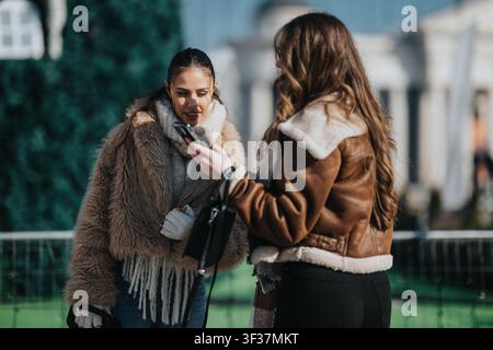 Due amici con giacche invernali che controllano un telefono e condividono un momento leggero e divertente all'aperto Foto Stock
