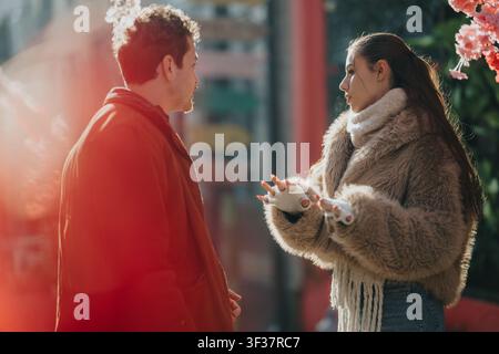 Due amici che hanno una conversazione informale su una strada invernale soleggiata, indossando cappotti caldi e sciarpe Foto Stock