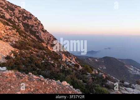 La luce dorata del tramonto bagna una costa montuosa frastagliata con una strada tortuosa che conduce verso isole lontane e un mare calmo, evocando solitudine avventura un Foto Stock
