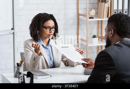Responsabile del personale serio che prende il resume dal candidato giovane di lavoro sopra intervista di lavoro presso l'ufficio aziendale moderno Foto Stock
