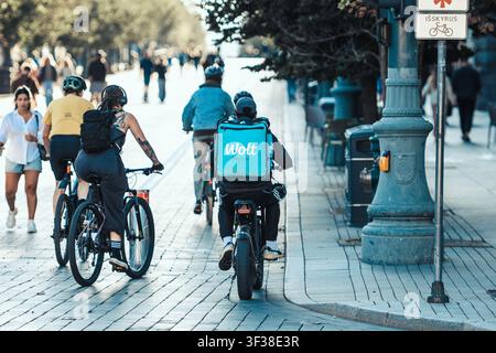 Corriere di consegna Wolt in bicicletta elettrica che trasporta oggetti in uno zaino blu chiaro del marchio Foto Stock