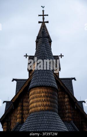 Vista drammatica verso l'alto della torre della chiesa di Heddal a Telemark, in Norvegia, che mostra intricate tegole di legno e croci su un cielo nuvoloso Foto Stock