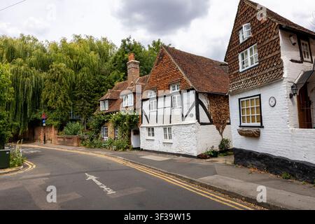 Una fila di cottage storici in legno a graticcio e rivestiti di tegole lungo una strada tranquilla a Godalming, nel Surrey, ombreggiata da un grande salice. Foto Stock