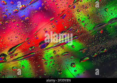 Gocce d'acqua colorate su sfondo astratto iridescente. Vista macro delle gocce d'acqua, superficie iridescente vivida con riflessi rossi e verdi Foto Stock