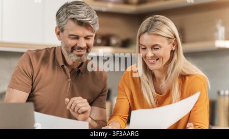 Coppia felice di mezza età che esamina documenti a casa, atmosfera rilassata, concetto aziendale Foto Stock
