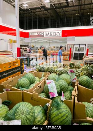 PLANO, TX, USA - 19 LUGLIO 2026: Acquirenti sfogliano vicino alla panetteria Kirkland all'interno di un negozio Costco, con angurie e ananas in esposizione in primo piano Foto Stock