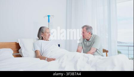 Anziano, coppia e visita seria al letto d'ospedale per preoccupazioni di recupero, complicazione chirurgica o ansia. Matrimonio, persone anziane e conversazione nel reparto clinico Foto Stock