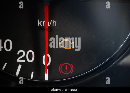 Una vista ravvicinata dettagliata di una spia arancione del controllo motore e di un freno a mano rosso sull'indicatore di avvertimento illuminato sul tachimetro del cruscotto di un'auto. Foto Stock